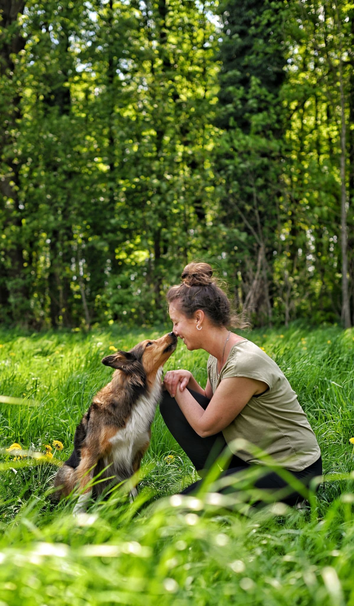 Marion kniet im Grünen und begegnet ihrem Hund auf Augenhöhe
